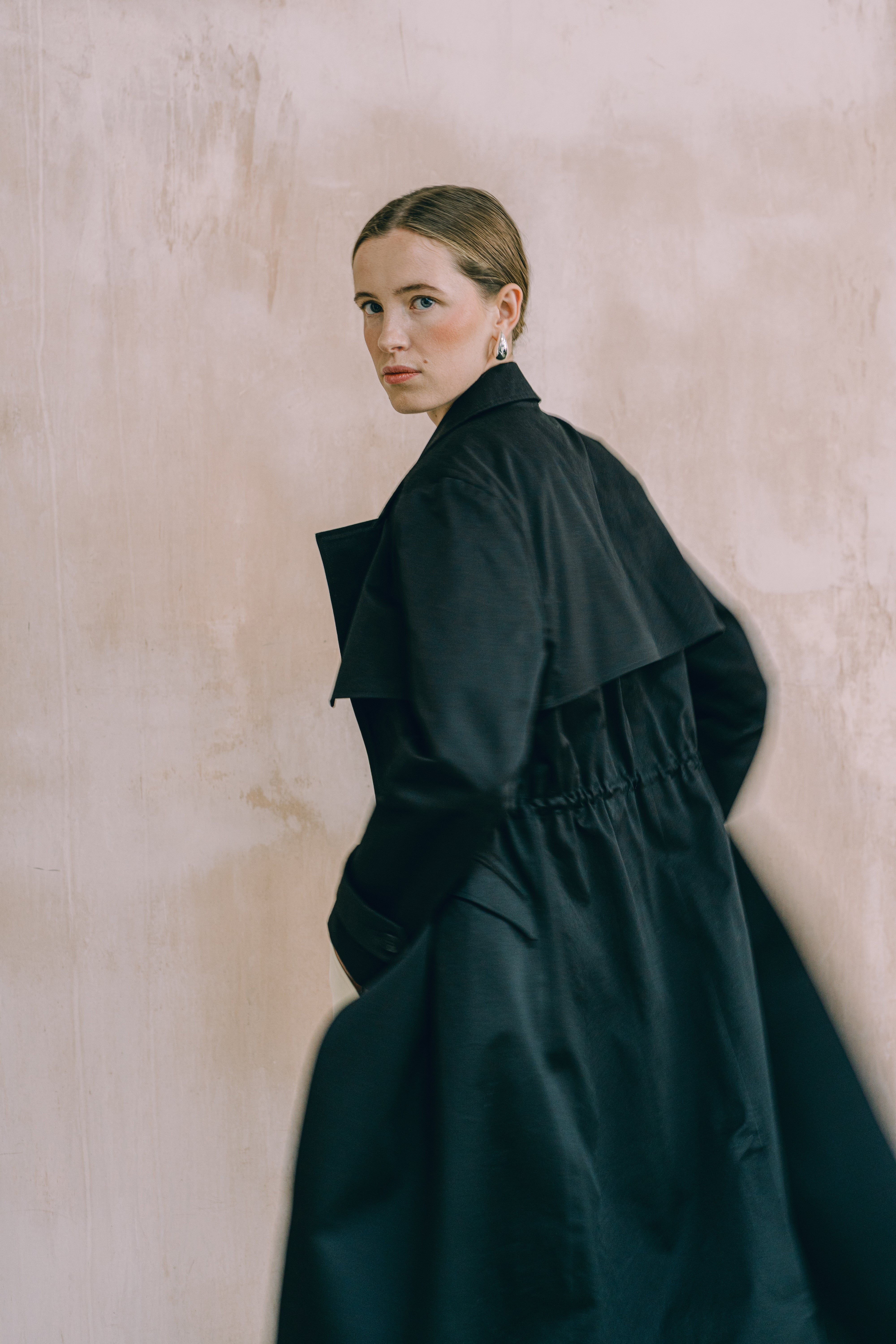 Woman wearing a black coat against a beige wall