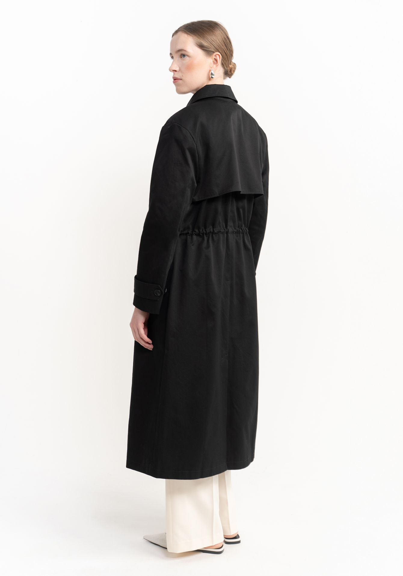 Woman wearing a black trench coat on a white background - back view