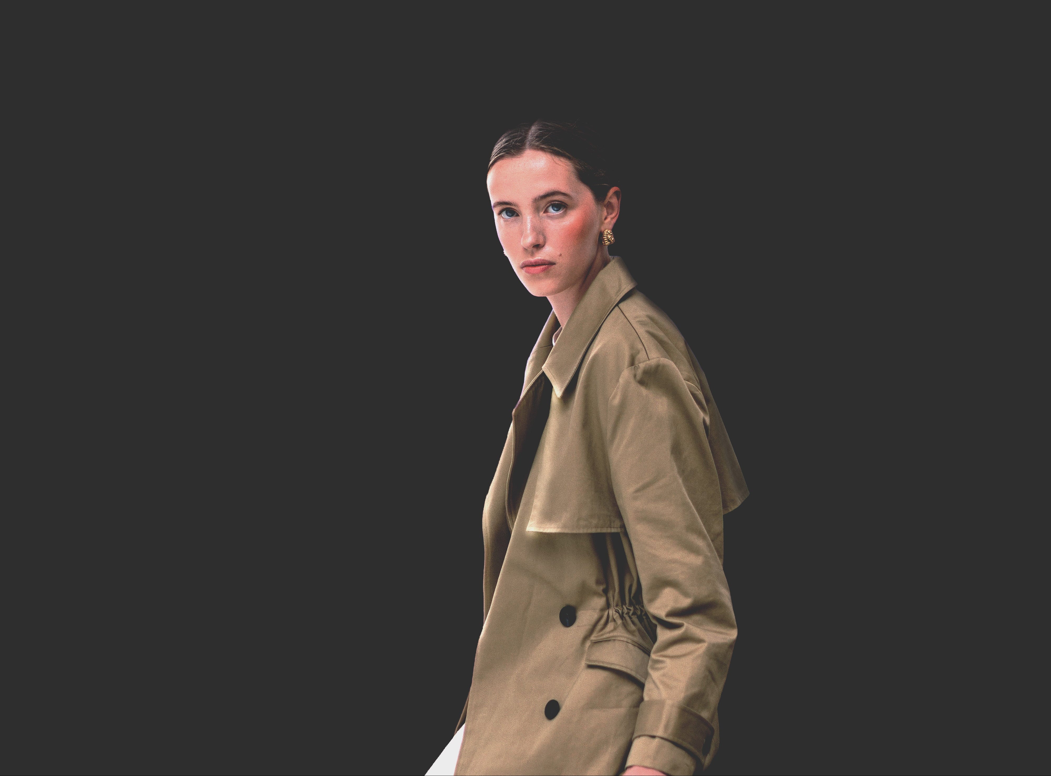 Woman wearing a beige trench coat against a black background