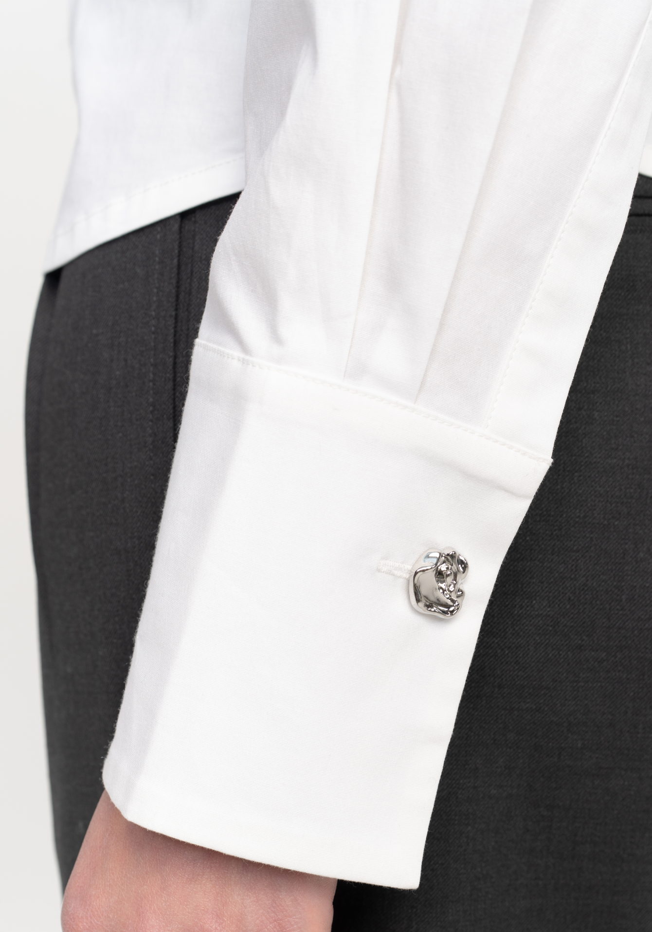 Close-up of a white blazer cuff with a silver cufflink on a grey trouser background