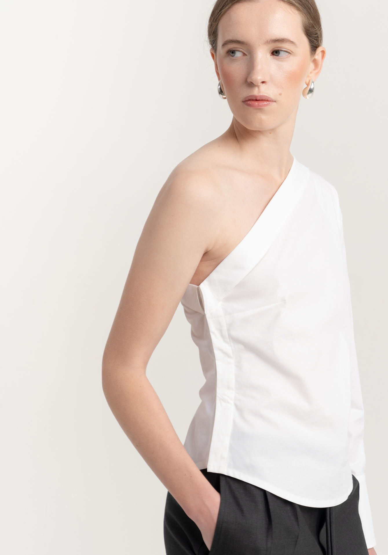 Woman wearing a white one-shoulder top against a plain background - close up