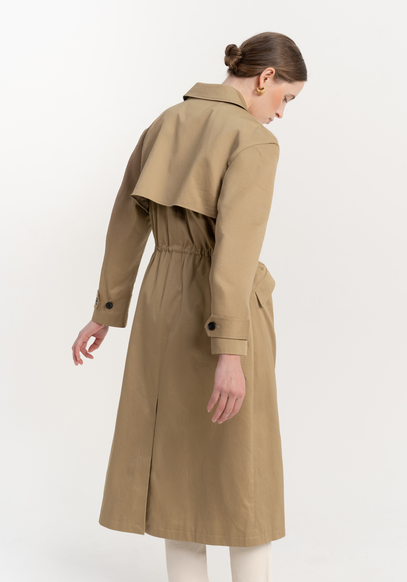 Woman wearing a beige trench coat on a white background - back view