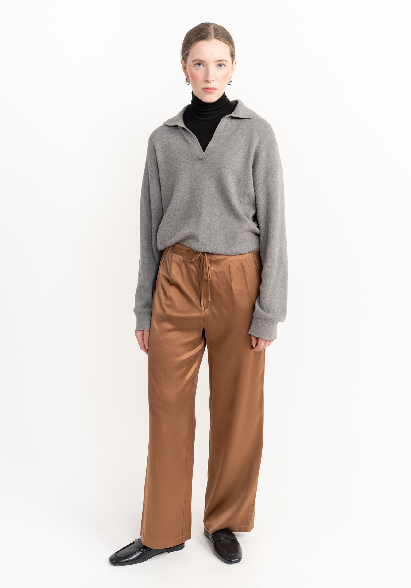 Woman wearing a gray sweater and brown silk trouser on a white background - front facing