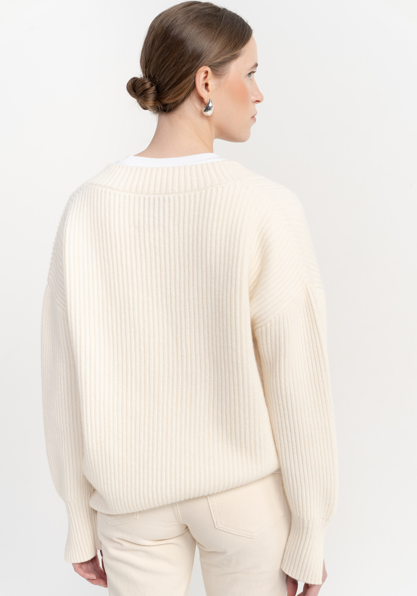 Woman wearing a cream ribbed sweater and pants on a white background - back view