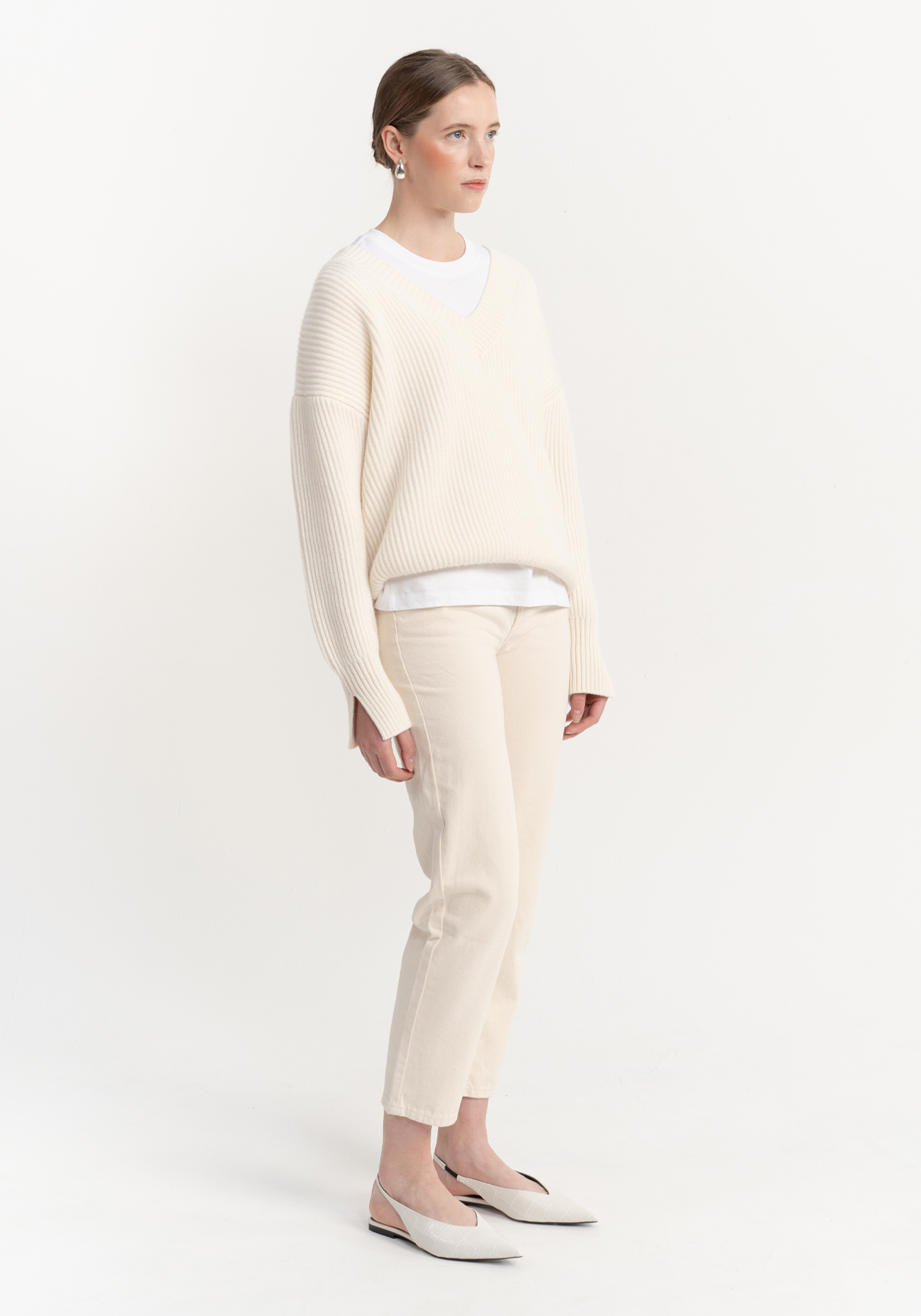 Woman wearing a cream-colored v neck knitted jumper on a white background - side view