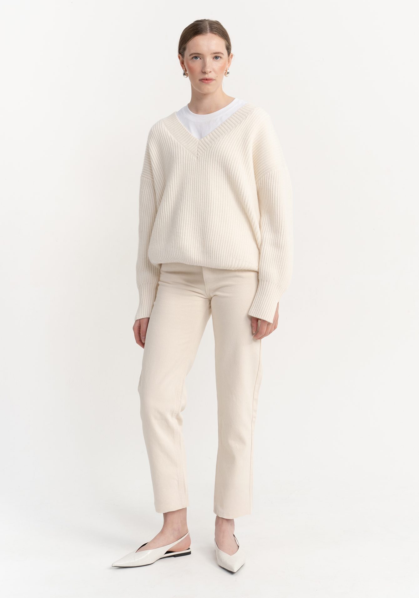 Woman wearing a cream sweater and jeans on a white background - front view