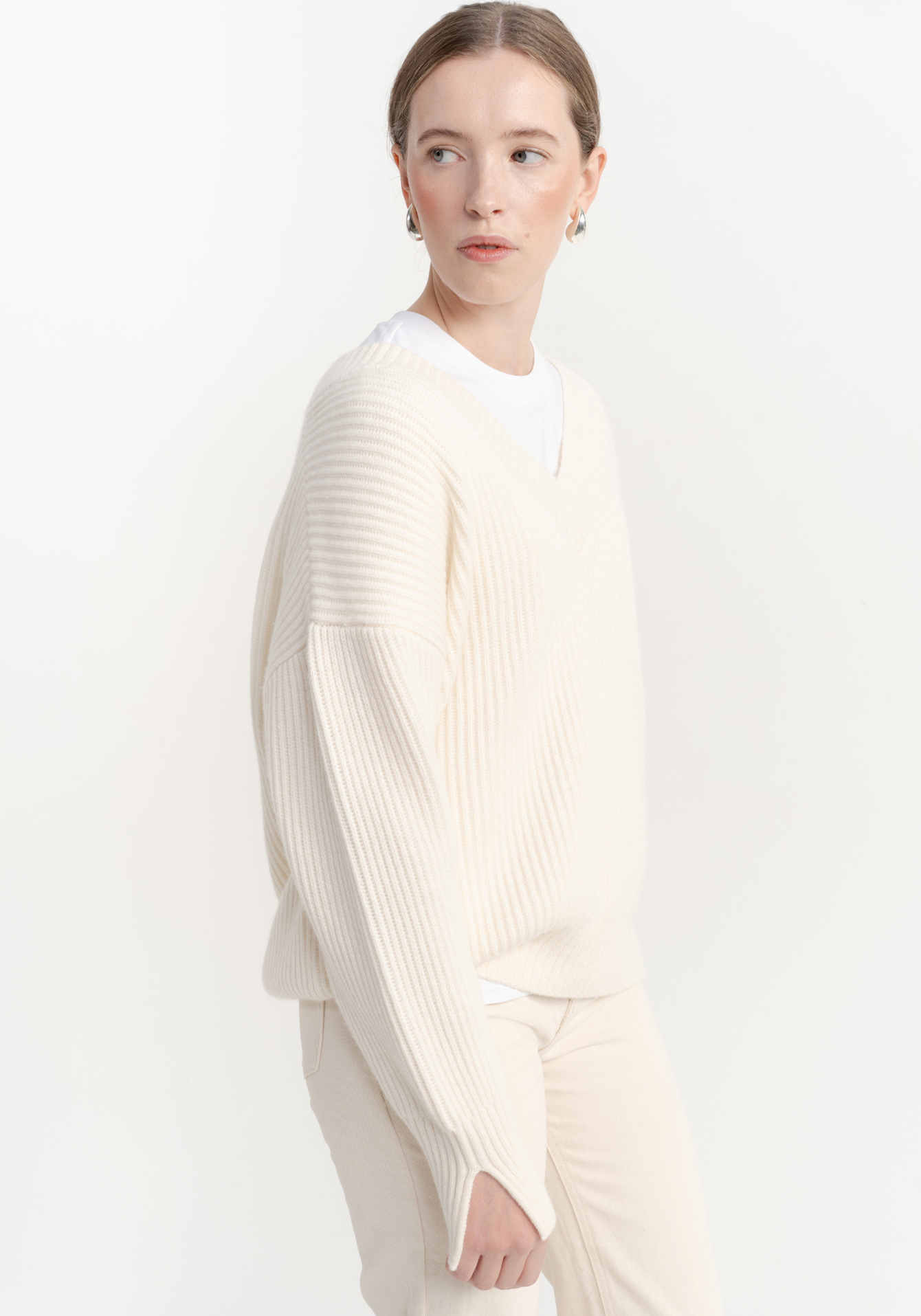 Woman wearing a white ribbed sweater on a plain background - side close view