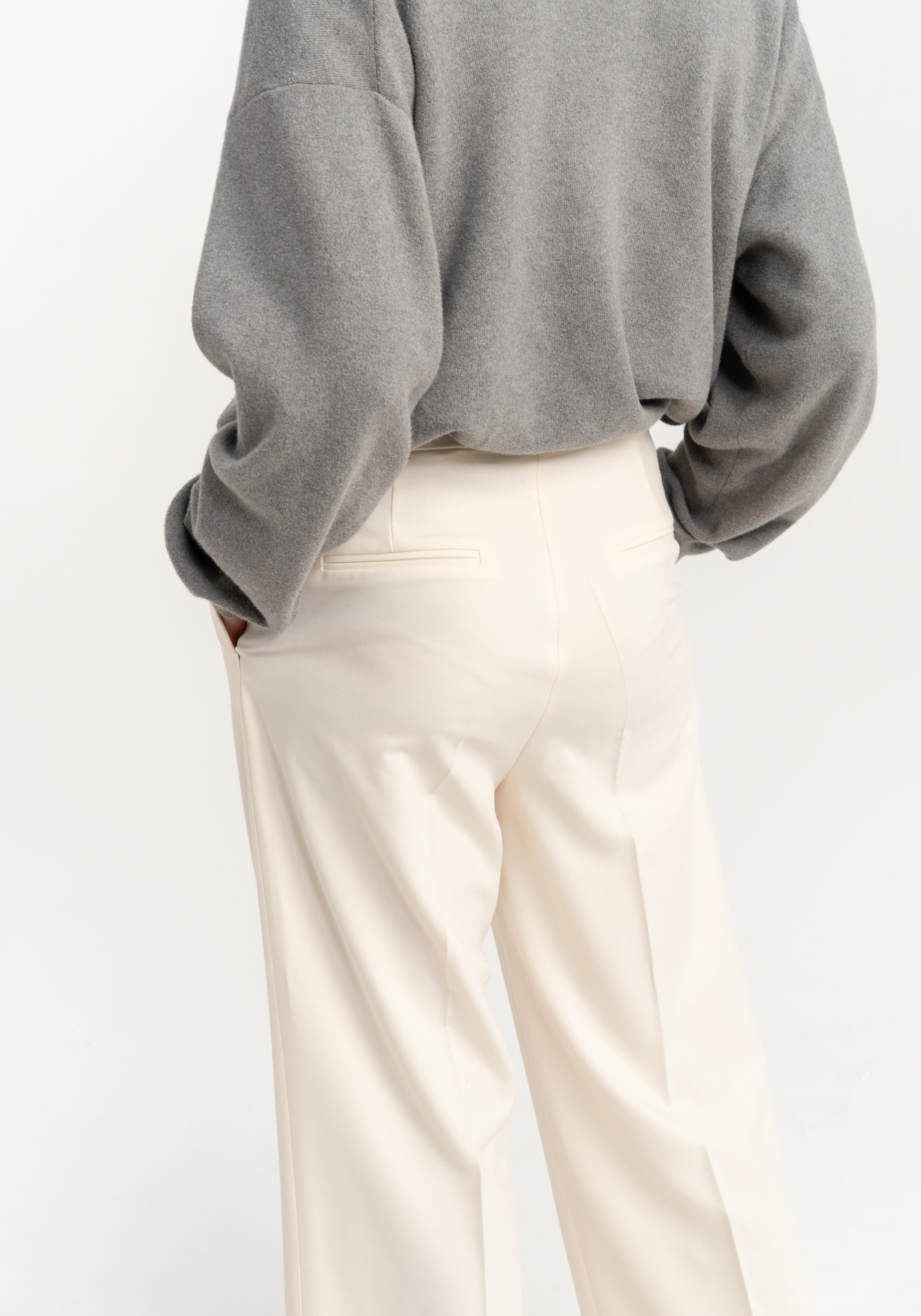 Person wearing a gray sweatshirt and creame trousers on a white background - back view