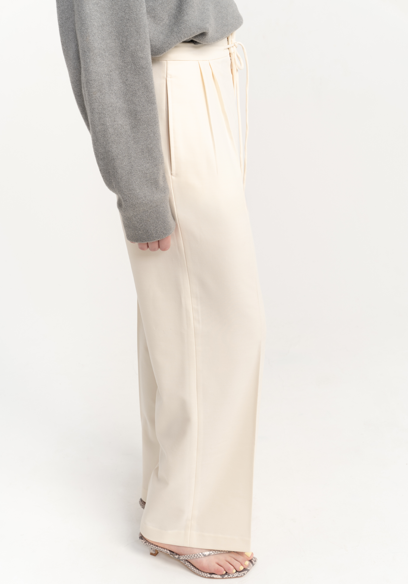 Person wearing beige trousers and a gray top on a white background - close up