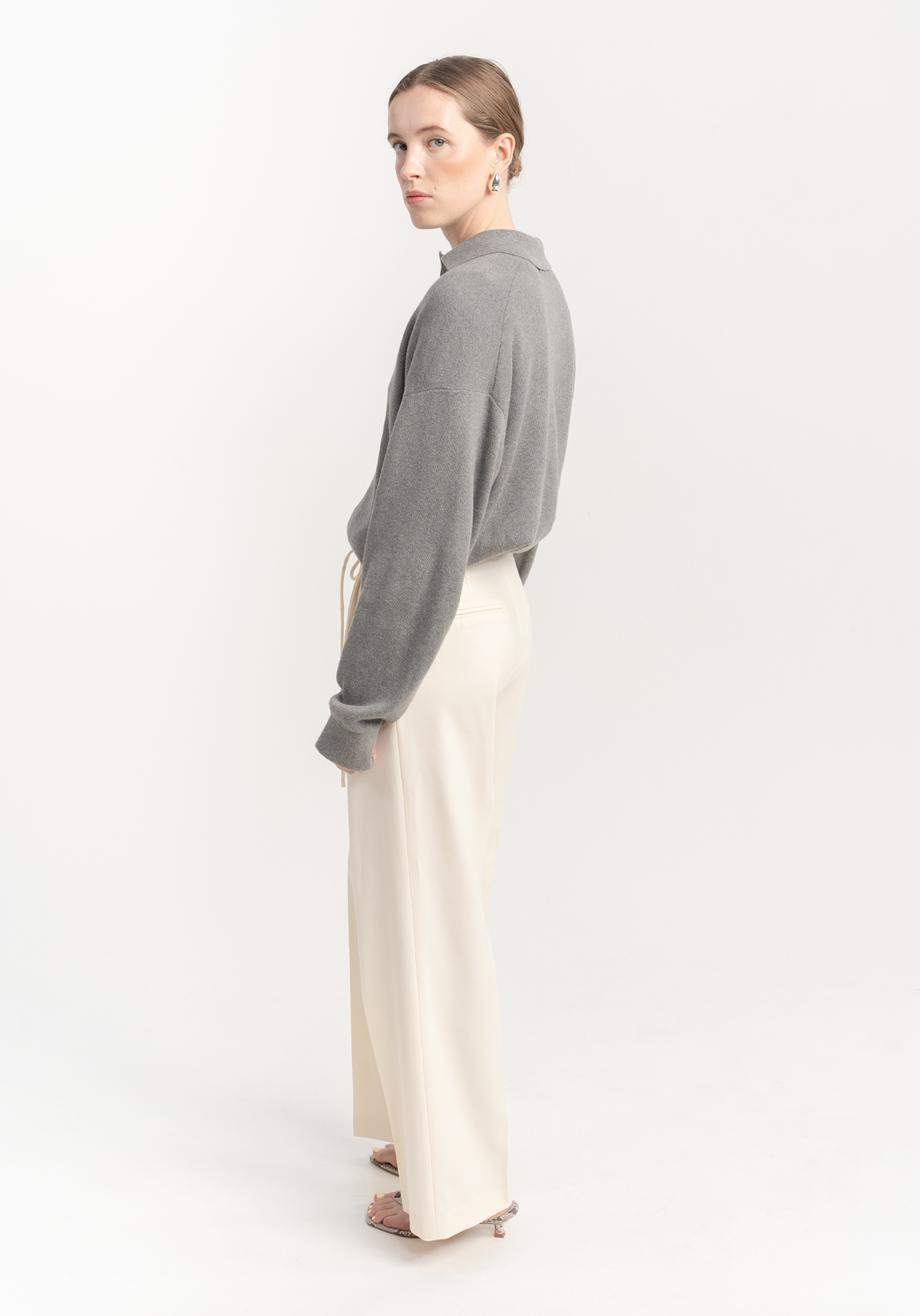 Woman wearing a gray sweater and cream trousers on a white background - side view