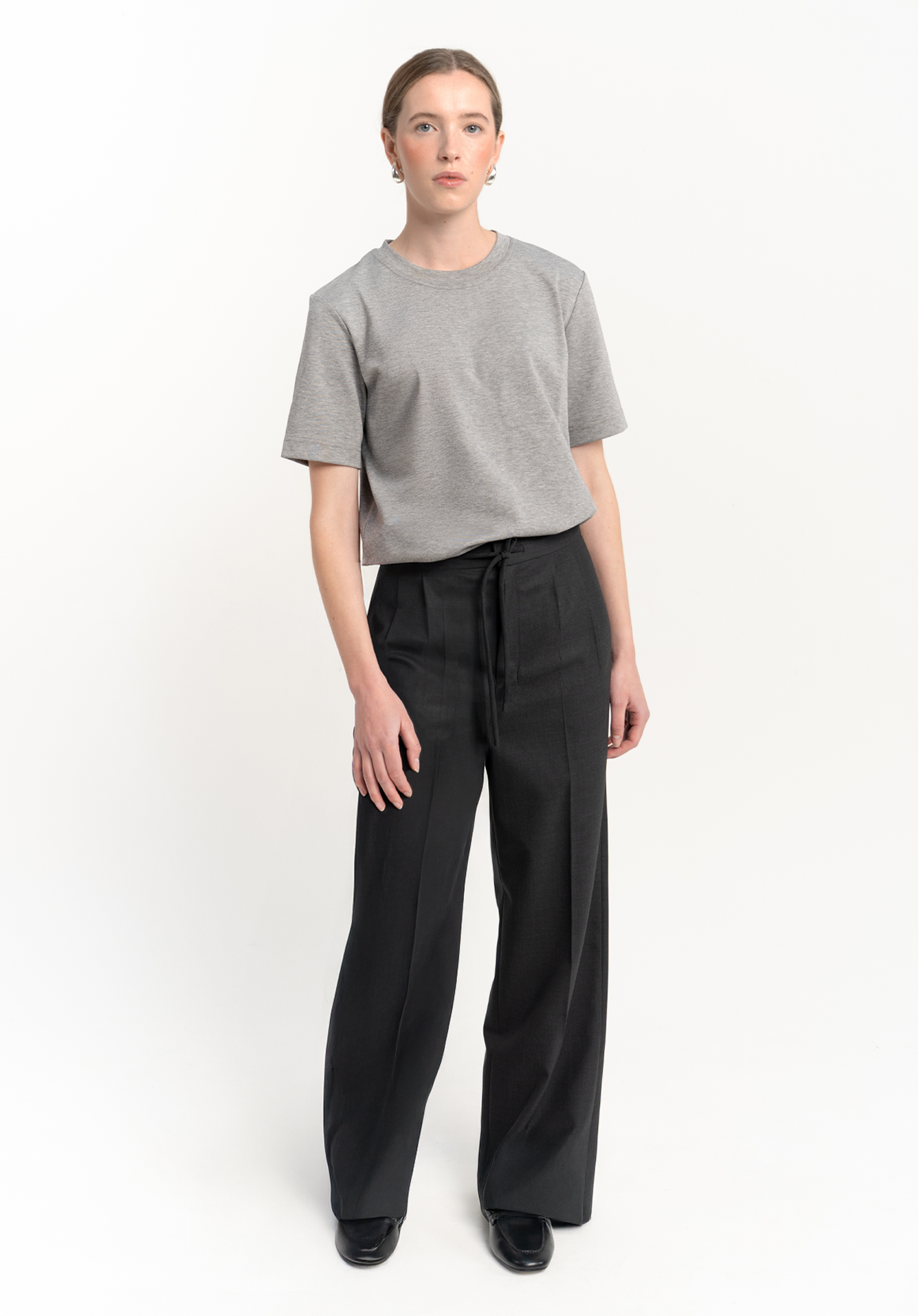 Women wearing a gray t-shirt and dark grey trousers on a white background - front view