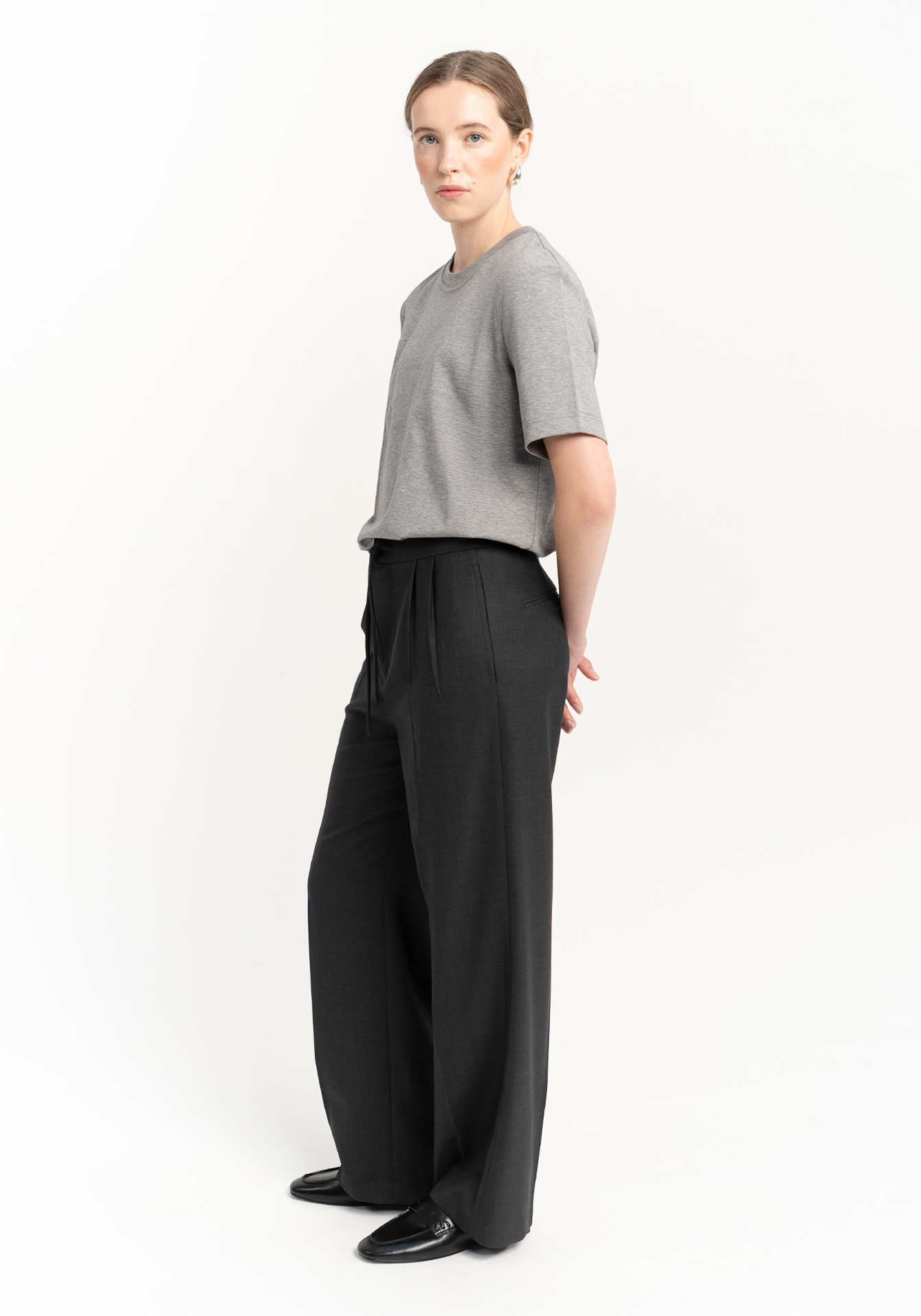 women wearing a white shirt and dark gray wide-leg trousers on a white background - looking at the camera