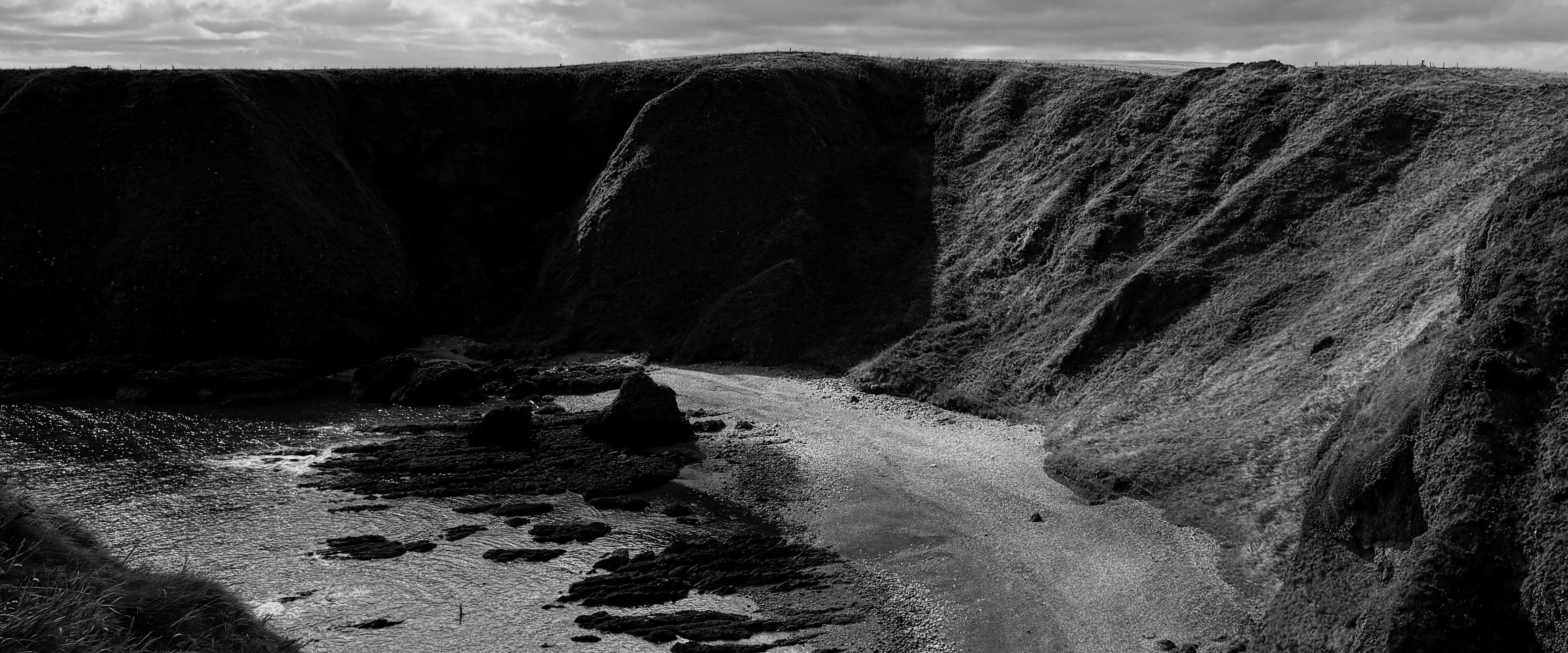 Black and white landscape of a coastal area with cliffs and a cloudy sky.