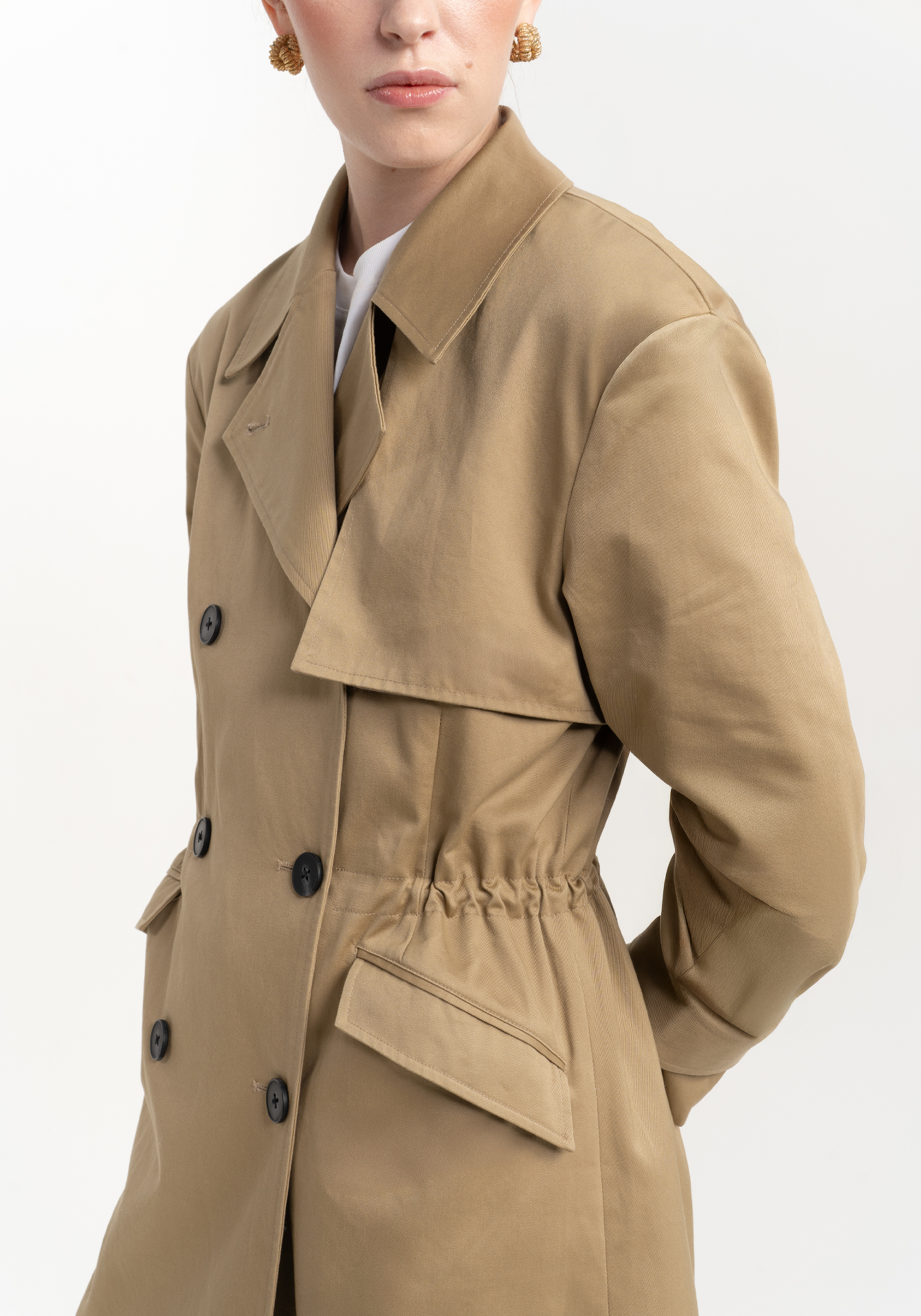 Beige trench coat worn by a person on a white background - close up 