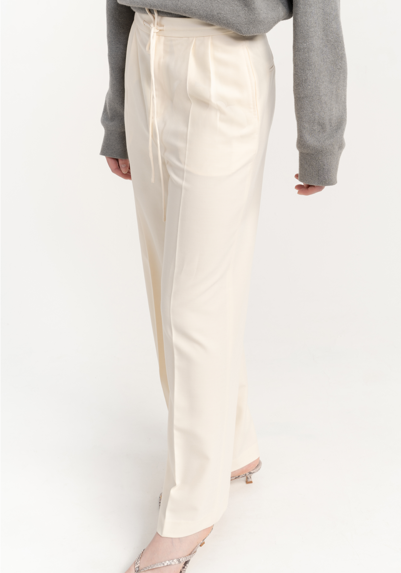 Person wearing cream trousers with a gray top on a white background- side view
