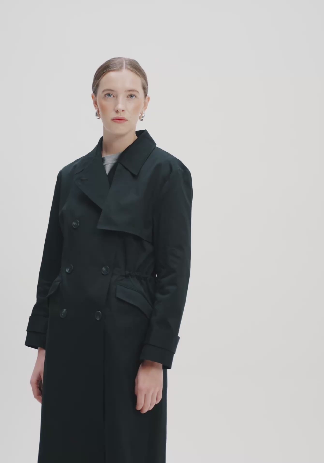 women in black trench coat in a white light studio 