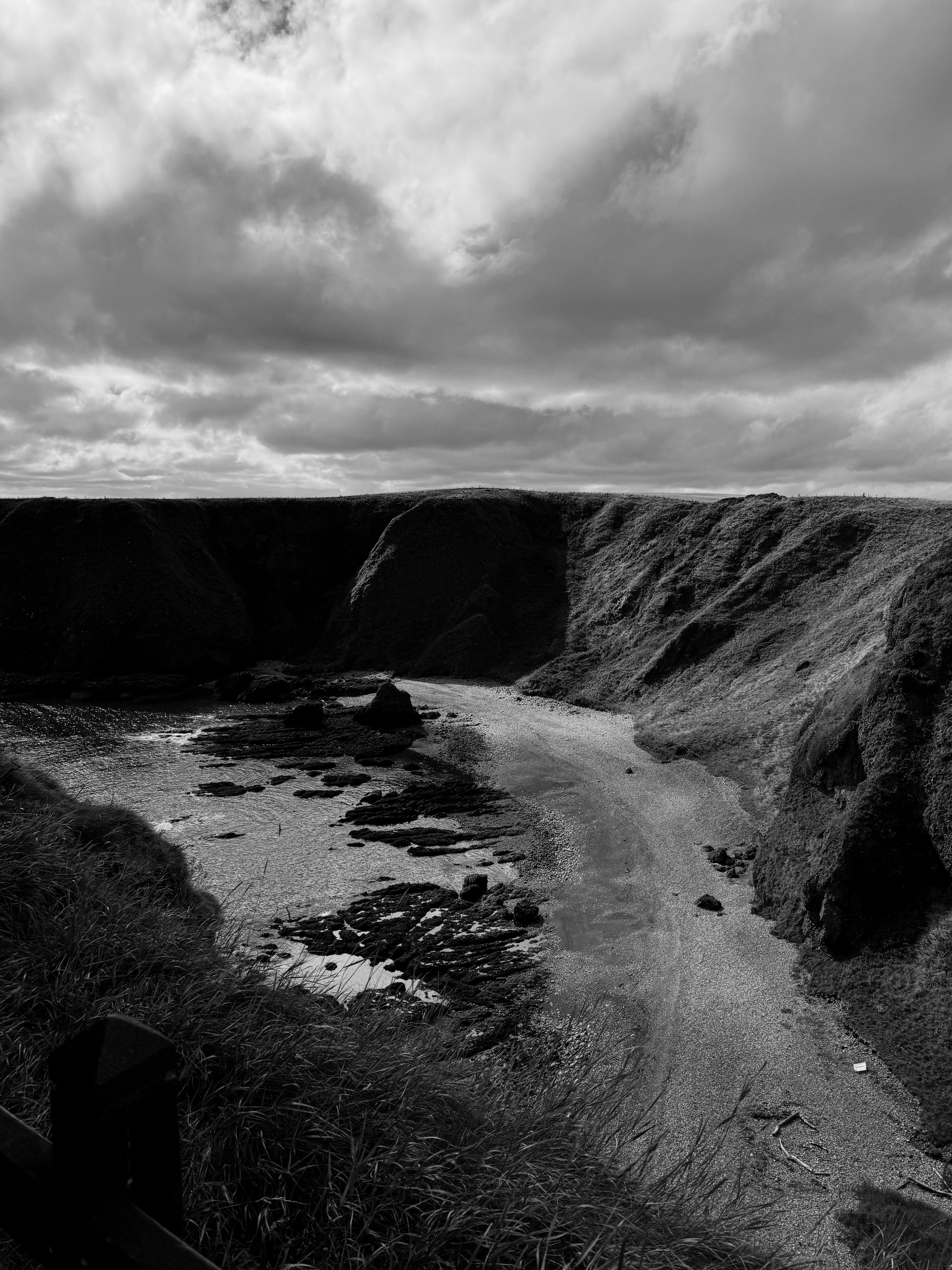 Black and white landscape of a coastal area with cliffs and a cloudy sky.